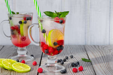 Fresh homemade summer cocktails with ice, lime and berries in glasses with a straw, copyspaceの写真素材