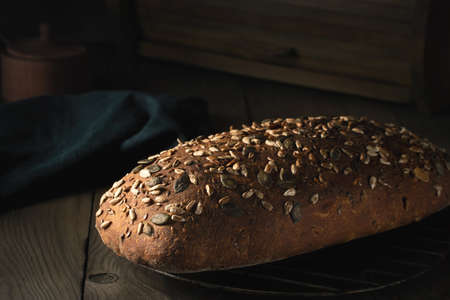 Loaf of homemade whole grain bread with seeds cool down on a wire rack on a wooden tableの写真素材