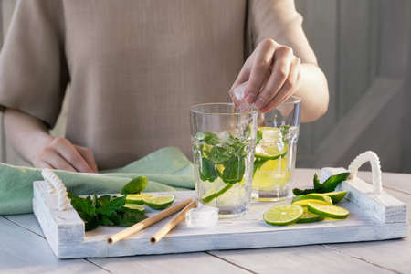 Girl prepares summer refreshing mojito fruit cocktails with lime and mintの写真素材