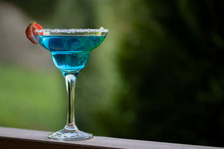 Glass with blue margarita cocktail garnished with lime zest and strawberries, selective focusの写真素材