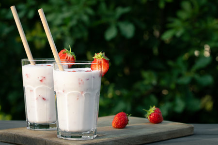Strawberry smoothie in two glass glasses and fresh strawberries on a wooden table in the yard, copyspaceの写真素材