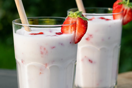 Strawberry smoothie in two glass glasses and fresh strawberries on a wooden table in the yard, close upの写真素材