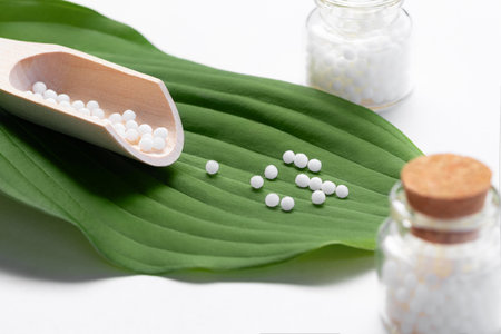 Homeopathic pills scattered from a wooden scoop on a green leafの写真素材