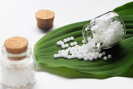 Homeopathic pills scattered from a bottle on a green leafの写真素材