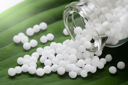 Homeopathic pills scattered from a bottle on a green leaf, close upの写真素材