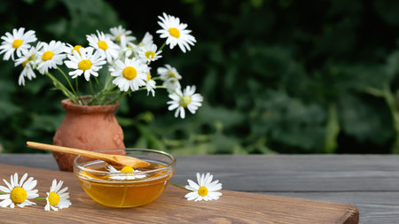 Chamomile syrup in a small bowl and in a jar in the patio on a wooden tableの写真素材