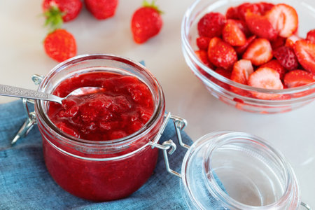 Glass jar with strawberry jam prepared for canning and fresh strawberries in a bowl on the tableの写真素材