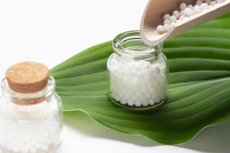 Pouring homeopathic granules from a wooden scoop into a bottleの写真素材
