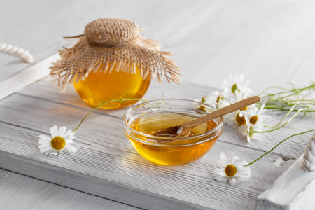 Chamomile syrup in a small bowl and in a jar on a white wooden tableの写真素材
