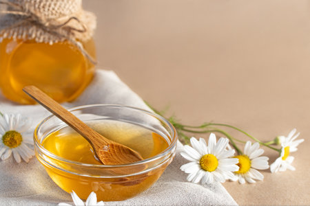 Chamomile syrup in a small bowl and in a jar and chamomile flowers on a linen kitchen towel, copy spaceの写真素材