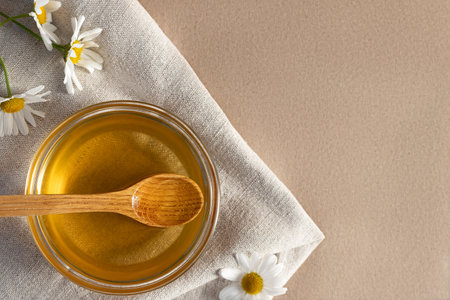 Chamomile syrup in a small bowl and in a jar and chamomile flowers on a linen kitchen towel, topview, copy spaceの写真素材