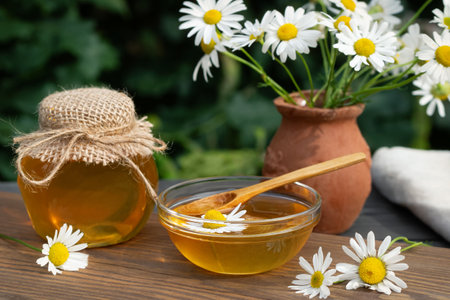 Chamomile syrup in a small bowl and in a jar in the patio on a wooden tableの写真素材