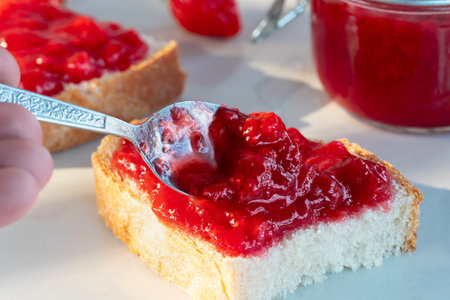Spreading strawberry jam on a piece of wheat breadの写真素材