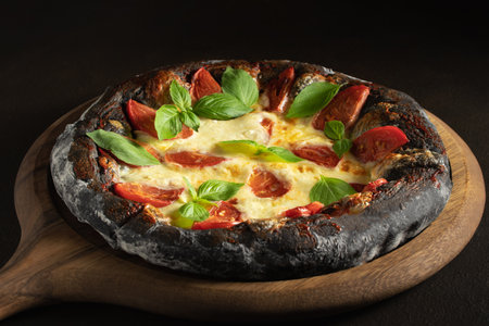 Black pizza margarita with tomatoes, mozzarella and basil. Dough with healthy bamboo charcoal powderの写真素材
