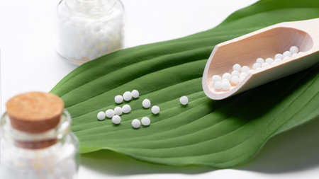 Homeopathic pills scattered from a wooden scoop on a green leafの写真素材