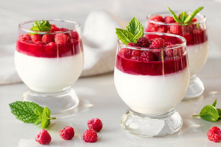 Panna cotta with raspberry jelly and mint leaves in glass glasses on a white tableの写真素材