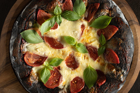 Black pizza margarita with tomatoes, mozzarella and basil. Dough with healthy bamboo charcoal powder, close upの写真素材
