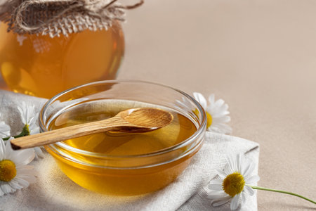 Chamomile syrup in a small bowl and in a jar and chamomile flowers on a linen kitchen towel, copy spaceの写真素材