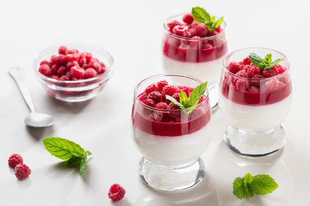 Panna cotta with raspberry jelly and mint leaves in glass glasses on a white tableの写真素材