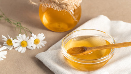 Chamomile syrup in a small bowl and in a jar and chamomile flowers on a linen kitchen towelの写真素材