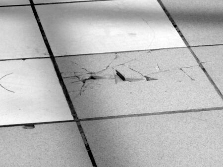 Black and white photograph of cracks in a tile floorの写真素材
