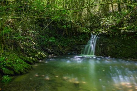 Sun ray lights over a small waterfall in a river in Galdames, Basque Country, Spainの写真素材