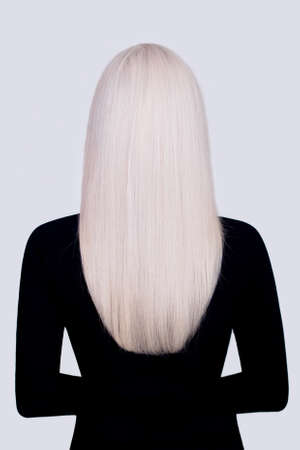 Female back with long, straight, healthy, blonde hair, in black dress, on gray backgroundの写真素材