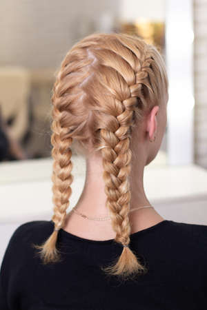 Female back with blonde braided hairstyle in hairdressing salon