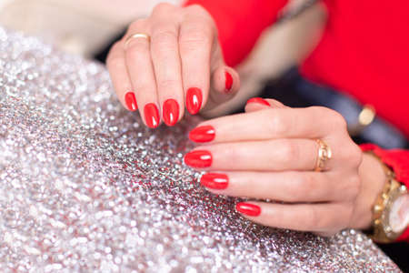 Close up view of beautiful female hands with luxury manicure nails, red gel polish, on sparkling...