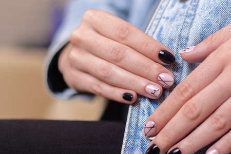 Close up view of beautiful female hands with fashion manicure nails, nude and black gel polish, on jeans backgroundの写真素材