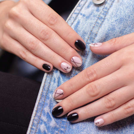 Close up view of beautiful female hands with fashion manicure nails, nude and black gel polish, on jeans backgroundの写真素材
