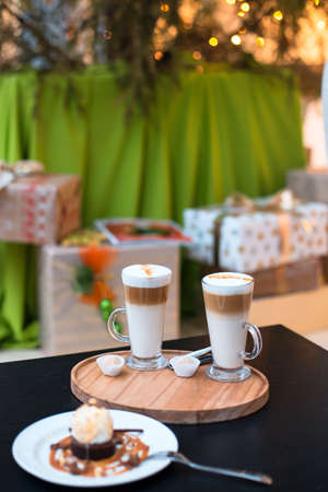 Two cups of coffee latte and cakes on Christmas tree and gifts backgroundの写真素材
