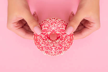 Female hands with pink manicure nails holding strawberry donut