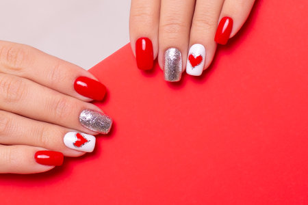 Beautiful female hands with stylish manicure nails, red gel polish, heart and Valentine's day design, with place for textの写真素材