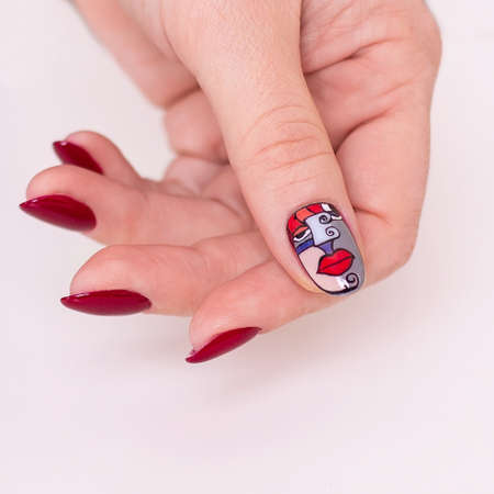 Beautiful female hand with creative manicure nails, red gel polish, lips design, white backgroundの写真素材