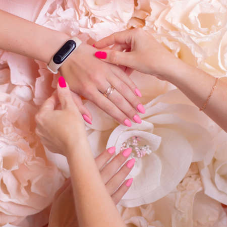 Nail master holding female manicure nails with pink gel polish for photo shoot on flower wall backgroundの写真素材