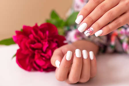 Beautiful female hands with romantic manicure nails, white gel polish, peonies flowers designの写真素材