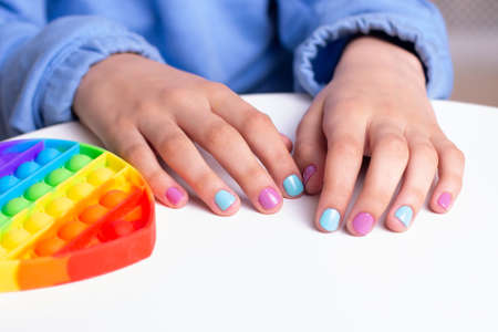 Little girl hands with beautiful manicure nails holding toy, pop itの写真素材