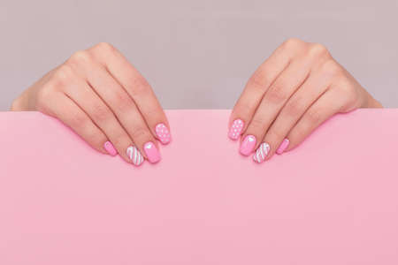 Beautiful female hands with fashion manicure nails, white gel polish, heart design, on pink background with place for textの写真素材