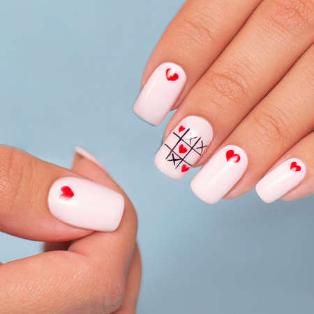 Beautiful female hands with romantic manicure nails, hearts and Valentine's day design, on blue backgroundの写真素材