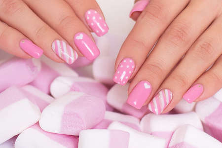 Female hands with pink manicure nails, hearts design on marshmallow backgroundの写真素材