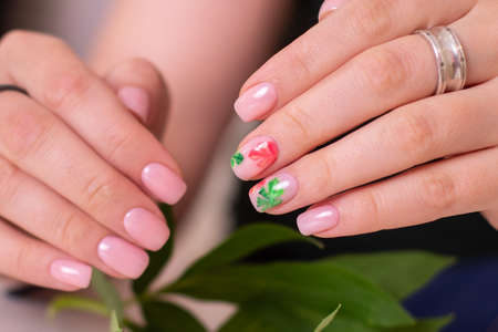 Beautiful female hands with creative manicure nails, nude gel polish, tropical leaves design