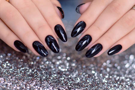 Beautiful female hands with fashion manicure nails, black gel polish, on glitter backgroundの写真素材