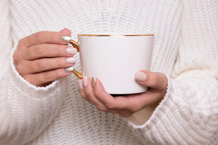 Beautiful female hands with beige manicure nails, holding cup of teaの写真素材