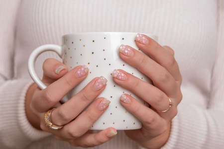 Beautiful female hands with festive manicure nails, holding cup of teaの写真素材