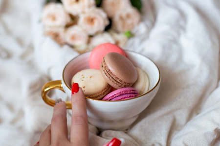 Sweet dessert, vanilla macaroons in mug and white roses on bed background. Romantic morning breakfast at bed.の写真素材