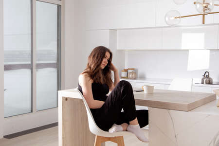 Young lonely brunette woman sitting in the kitchen and dreamingの写真素材