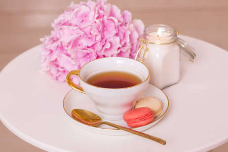 Cup of tea, macaroons, golden knife and fork and pink hydrangea flower on white tableの写真素材