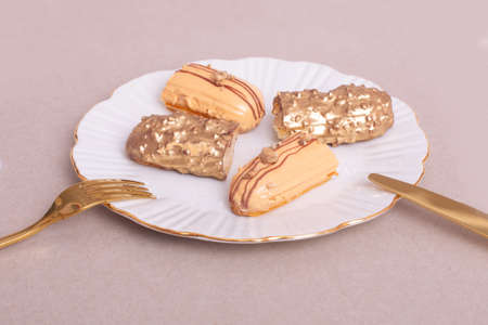 Golden colored eclairs on plate with knife and fork on gray backgroundの写真素材