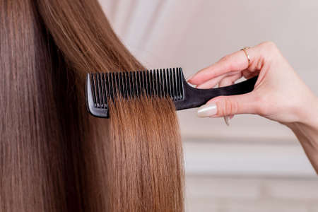 Hairdresser's hand brushing long brunette hair in beauty salon